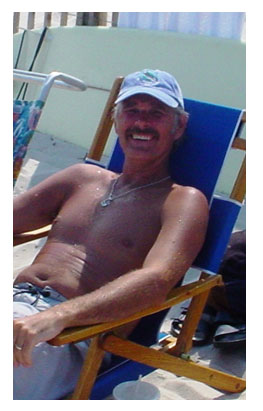 Photo of Mike sitting on the beach smiling.